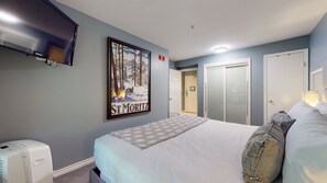 A hotel room with a bed, a wall-mounted TV, a poster, a heater, and a wardrobe.