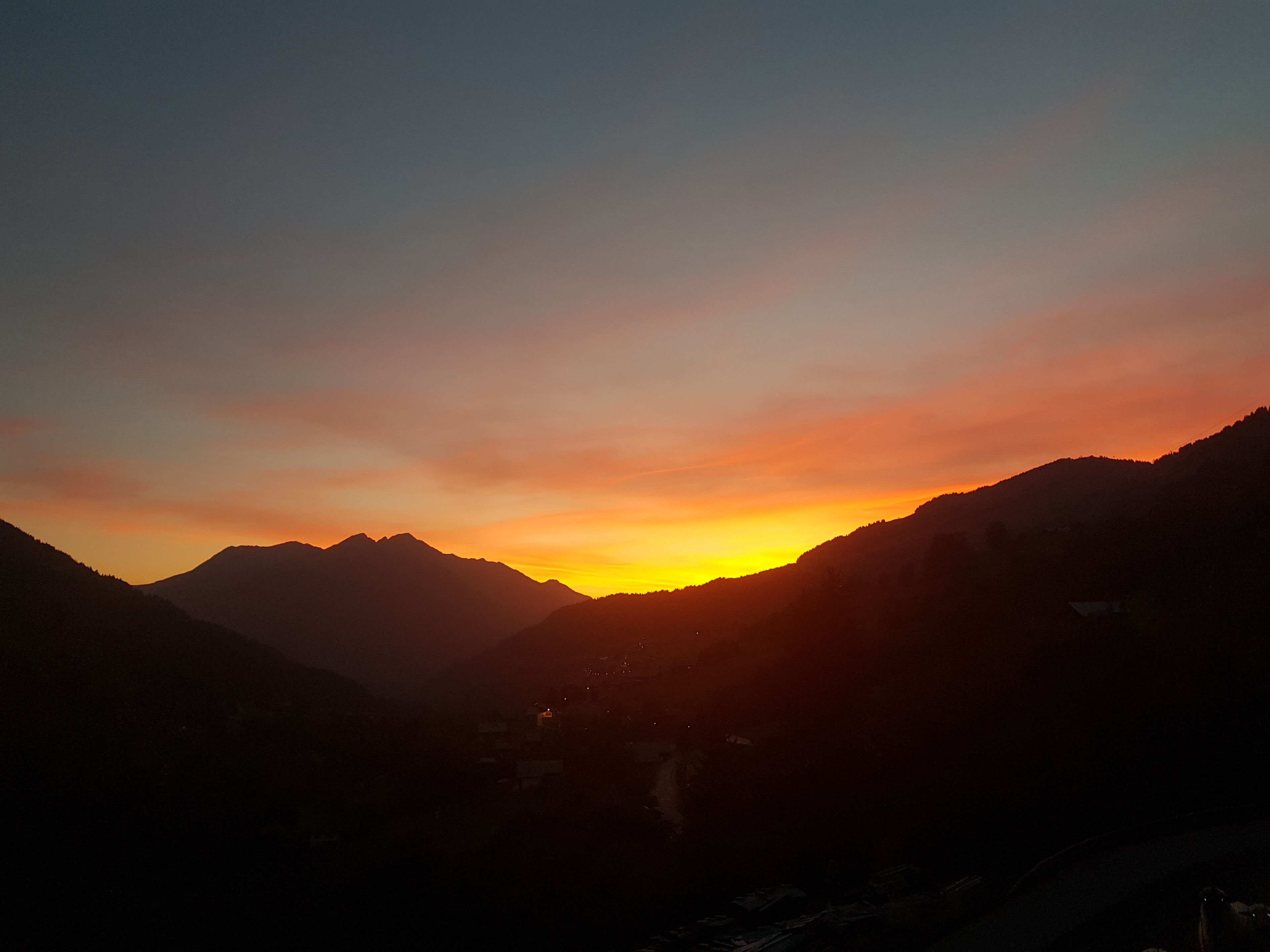 A mountainous landscape during sunset with silhouettes of mountains and a valley.