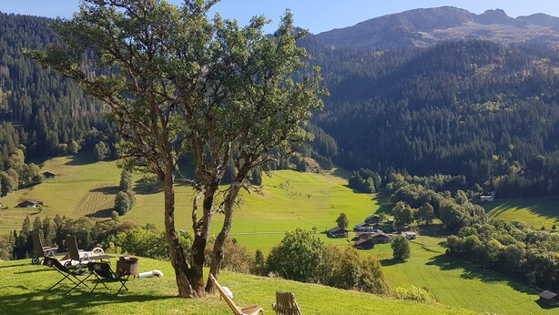 Ein grasbewachsener Hügel mit einem Baum, zwei Holzstühlen, einem kleinen Tisch und einem Zelt.