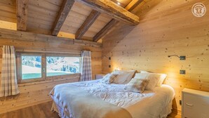 Ein Schlafzimmer einer Holzhütte mit einem großen Bett, einem Fenster mit Vorhängen und einem Nachttisch.