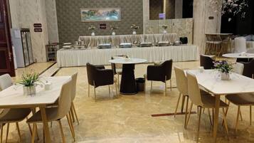 A hotel dining area with round tables, chairs, and a buffet setup.