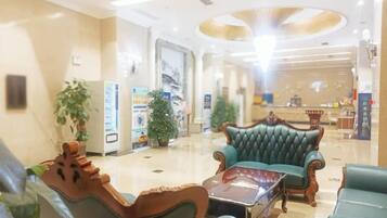 A hotel lobby with a reception desk, seating area, and a large plant.