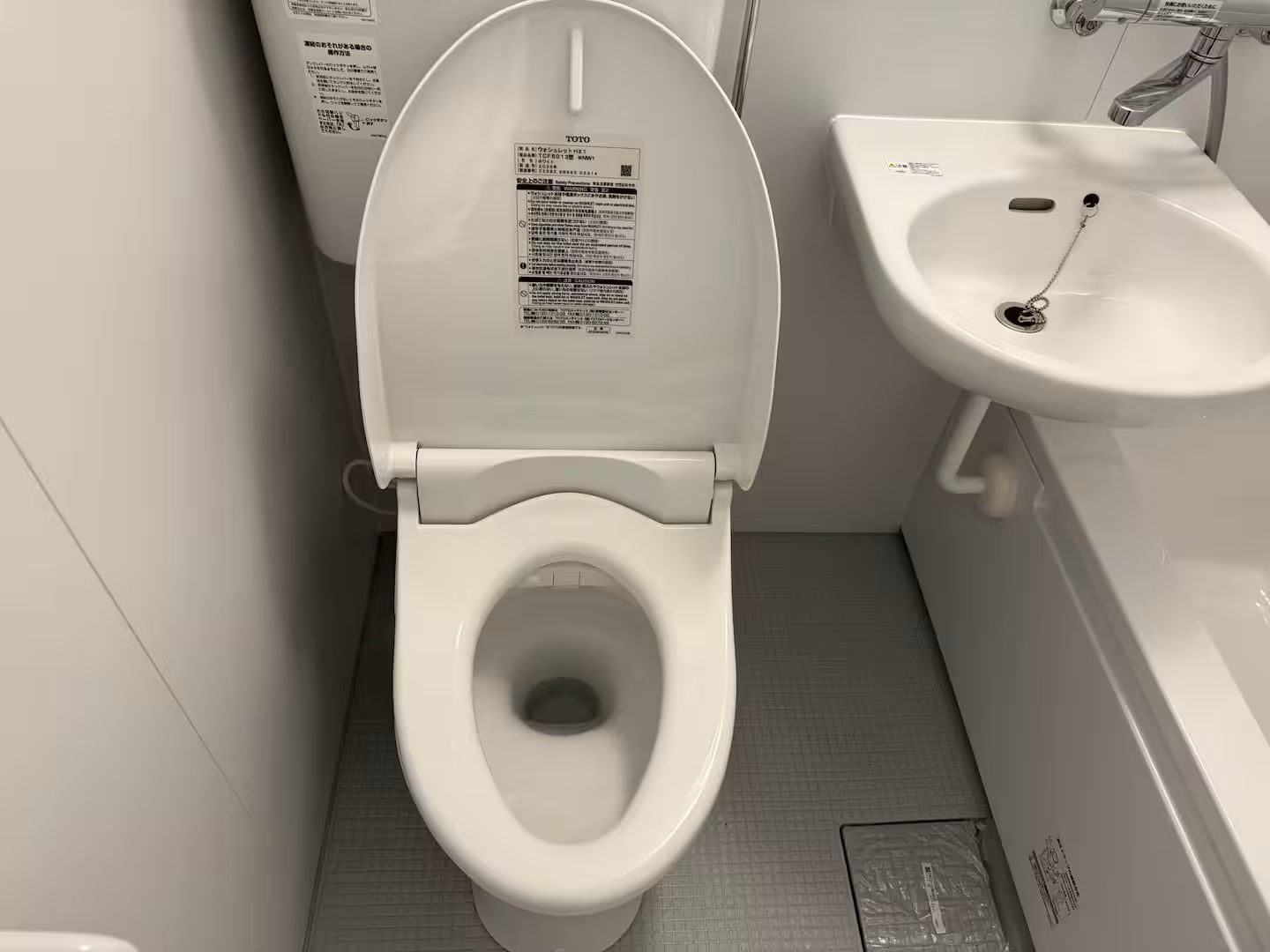 A white toilet with a TOTO label, a white sink with a faucet, and a tiled floor.
