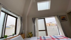A hotel room with a bed, two windows, a small skylight, and a view of buildings outside. - Quartier Blanc Yoga (Tokyo)