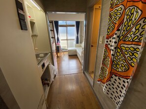 A narrow hallway with a kitchen area on the left, a white sofa in the center, and a patterned curtain on the right. - Quartier Blanc Yoga (Tokyo)
