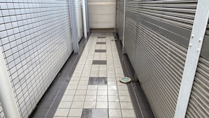 A narrow corridor with tiled flooring, metal shutters on the right, and a tiled wall on the left. - Quartier Blanc Yoga (Tokyo)