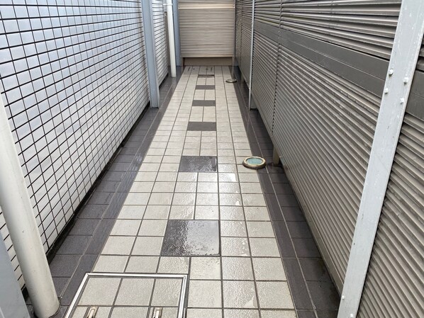 A narrow corridor with tiled flooring, metal shutters on the right, and a tiled wall on the left. - Quartier Blanc Yoga (Tokyo)
