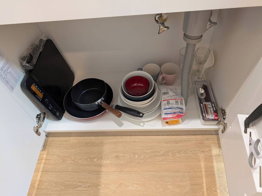 A kitchen counter with a rice cooker, frying pan, stack of plates, and a package of utensils.