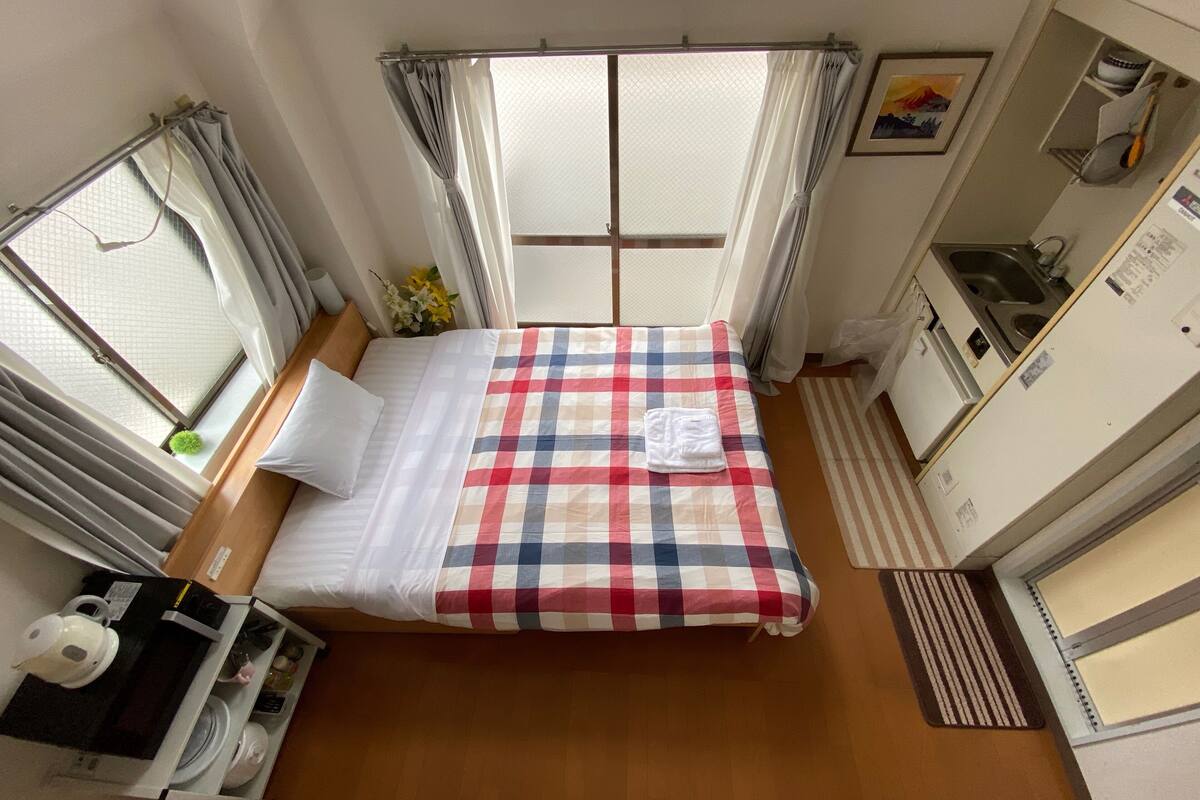 A compact hotel room with a bed, a small desk, a sink, and a window with curtains.