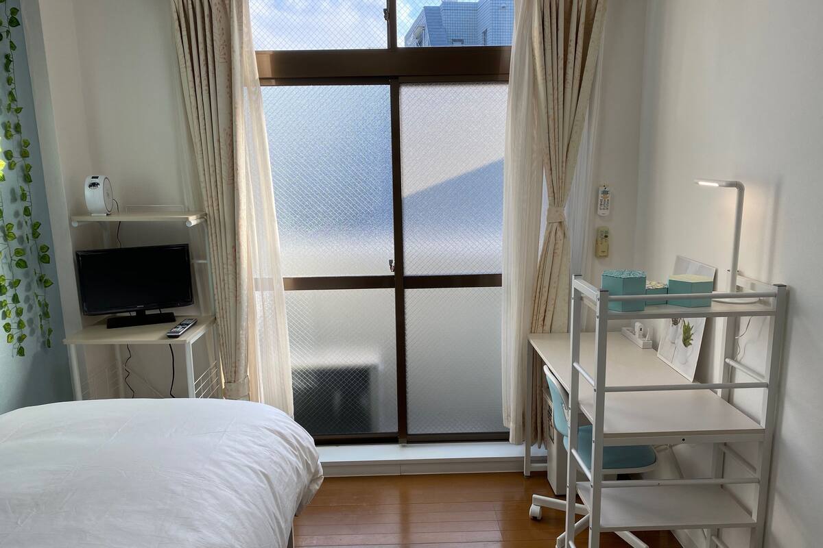 A hotel room with a bed, a desk with a computer, a TV, and a window with curtains.