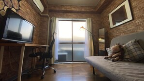 A room with a brick wall, a desk with a computer, a couch with a stuffed toy, and a large window. - Quartier Blanc Yoga (Tokyo)