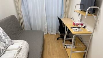 A compact room with a bed, a desk, and a TV on a shelf.