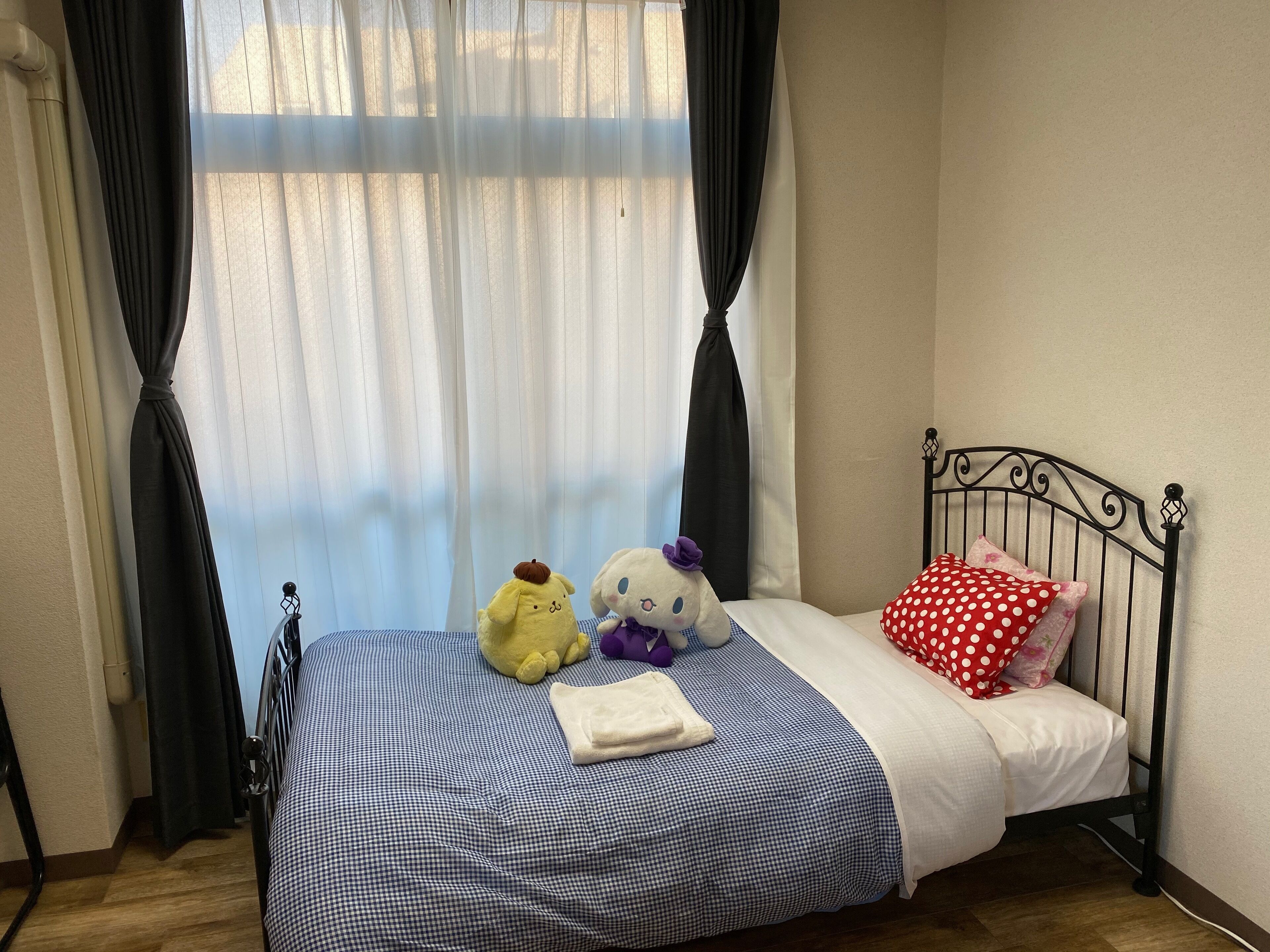 A bedroom with a bed, a window with curtains, and two stuffed animals on the bed.