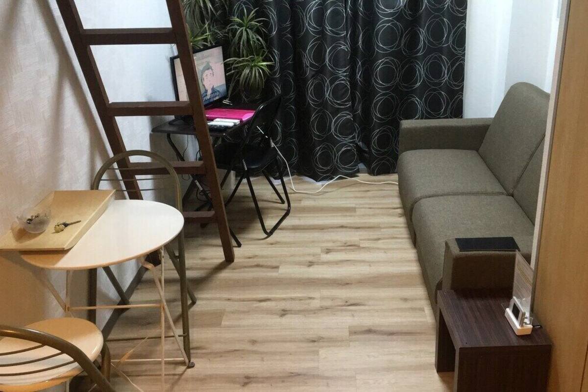A compact living space with a sofa, a small table, a chair, a ladder, and a desk with a computer.