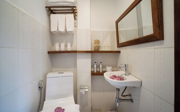 Un baño con inodoro, lavamanos y ducha. Hay toallas y artículos de aseo en estantes.