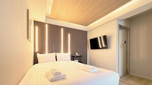 Habitación de hotel moderna con una cama grande, un televisor de pantalla plana montado en la pared y una puerta que da al baño.