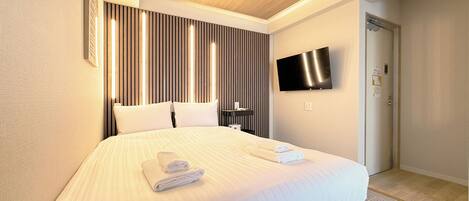 Ein modernes Hotelzimmer mit einem großen Bett, einem flachbildfernseher an der Wand und einer Tür zum Badezimmer.