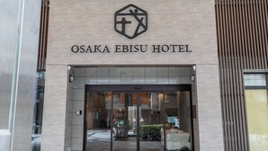La entrada al Hotel Osaka Ebisui, con un diseño moderno, presenta una amplia puerta de cristal y un felpudo de bienvenida.