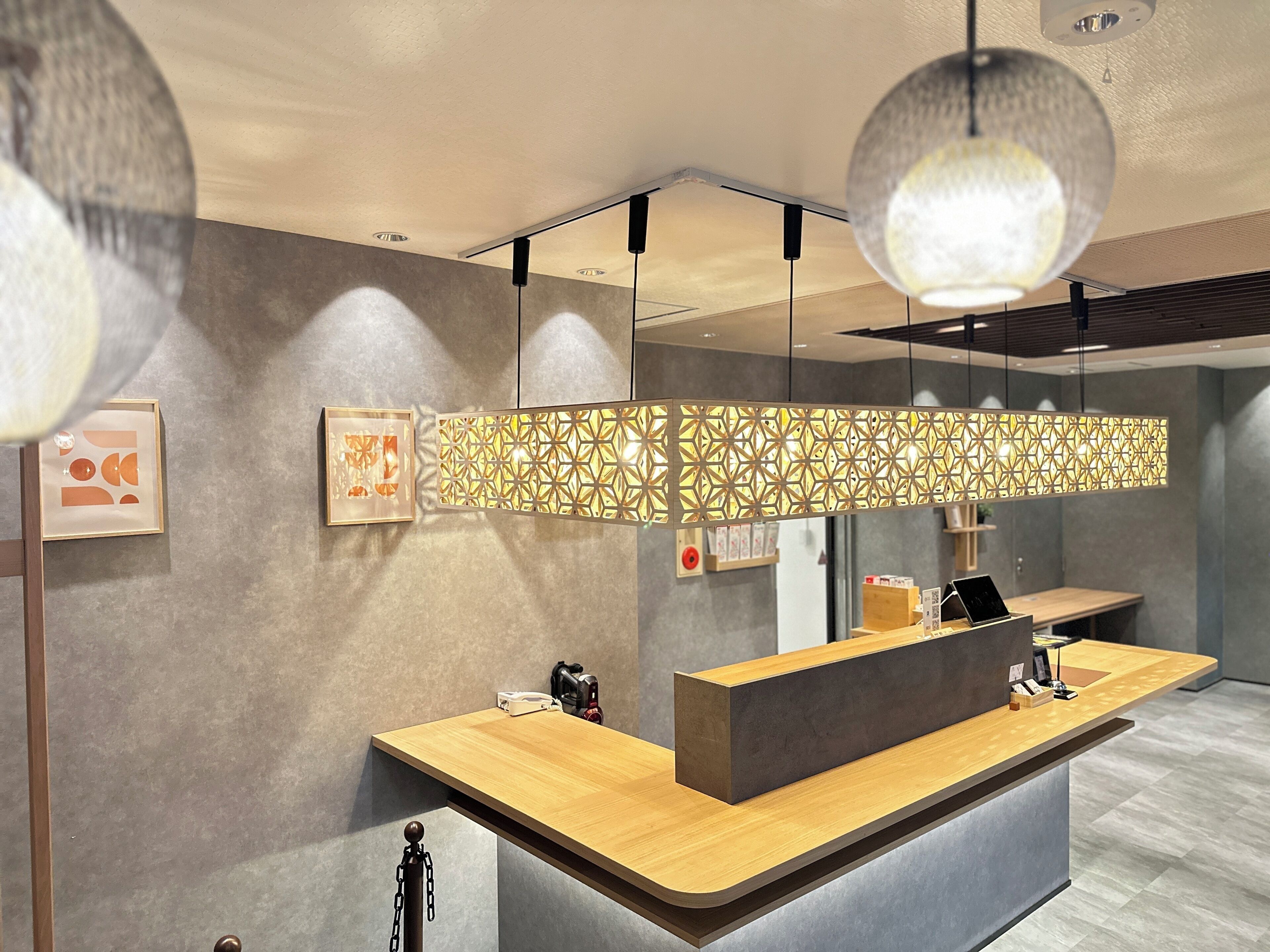 A modern reception desk with a wooden counter, a patterned decorative panel, and pendant lighting.