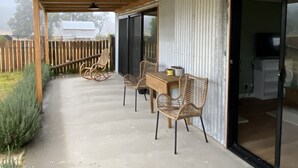 Katettu terassi, jossa on betonilattia, puupalkit ja lasiliukuovi, joka johtaa keittiötilaan.