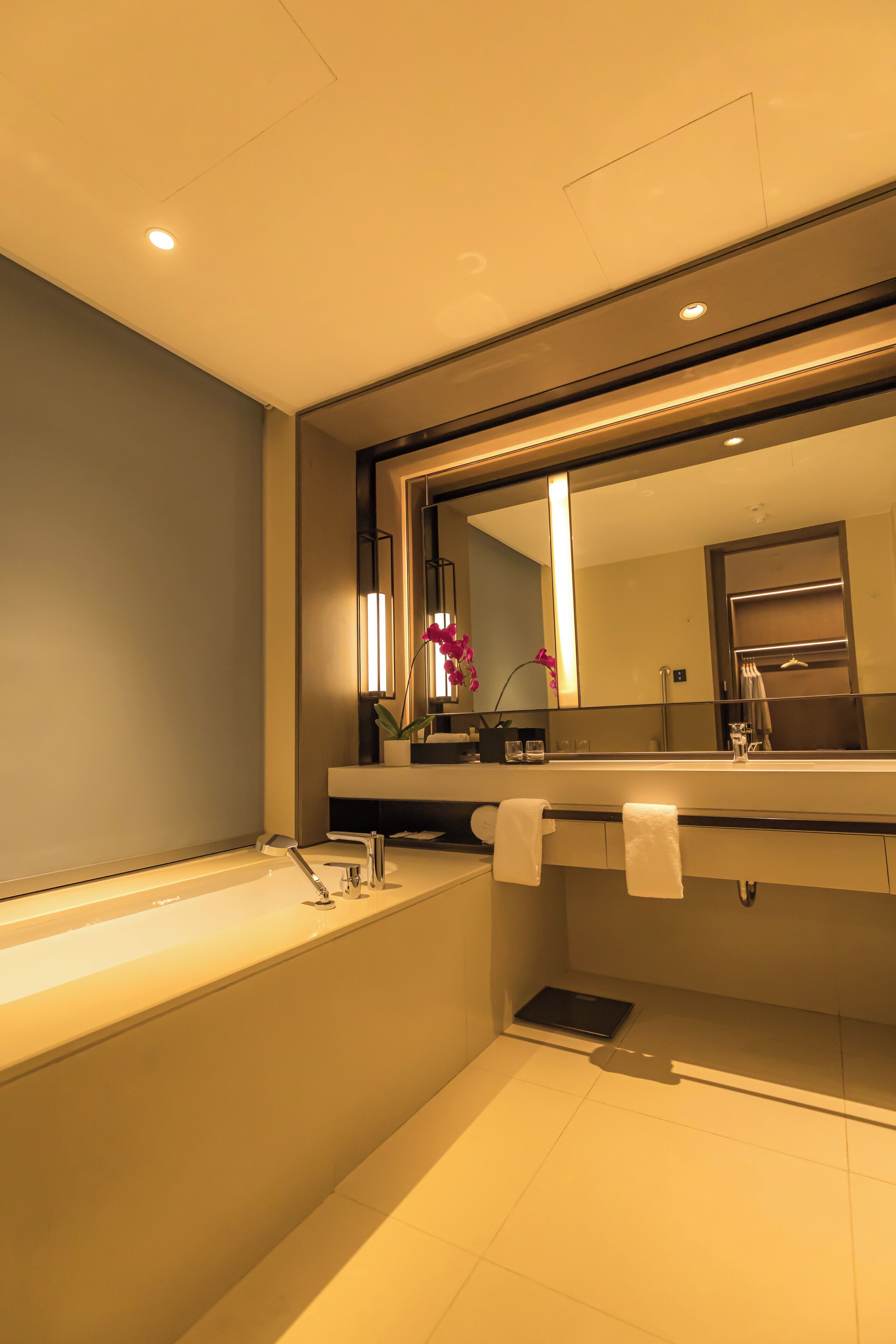 A modern bathroom with a large mirror, a bathtub, and a vanity with a sink.