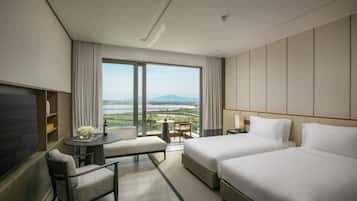 A hotel room with a large window, a bed, a desk, a chair, and a TV.