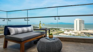 A balcony with a sofa, a round ottoman, and a small table with a bottle and glass. - Hoiana Residences (Da Nang)