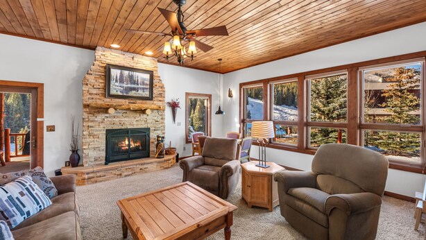 A cozy living room with a stone fireplace, wooden ceiling, and large windows offering a view of a snowy landscape. - Meridian Magic-Fantastic 4BD home, Dog friendly (Skyland & Surrounding Areas)