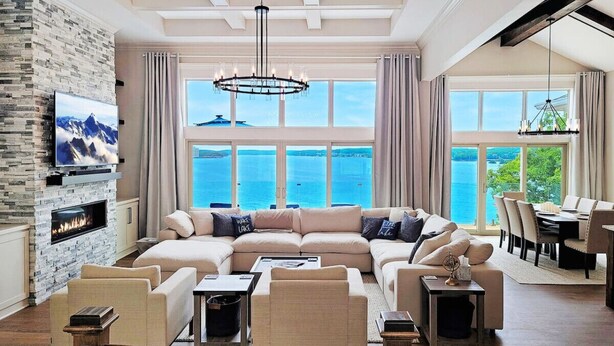 A spacious living room with a large sectional sofa, a fireplace, and a view of the sea. - *NEW* TV-Featured Mansion / Waterfront / Dock / Golf Green / Games (Sunrise Beach)