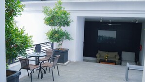 A covered outdoor patio with a table and chairs, a potted plant, and a view into a room with a sofa and armchairs. - Le Mansion Senopati Hotel (Jakarta)