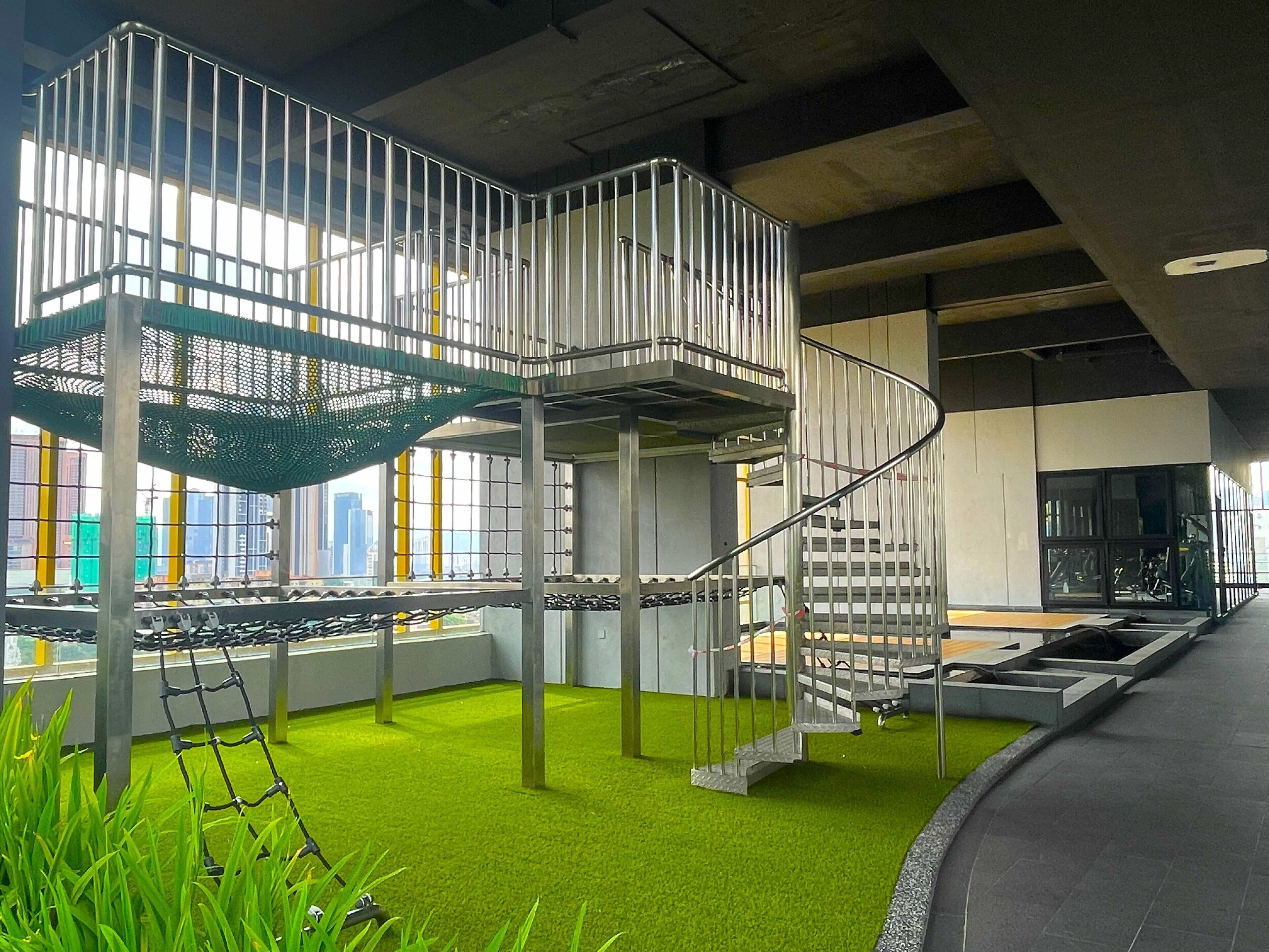 Un espacio interior moderno con una escalera en espiral, césped artificial y barandillas metálicas.
