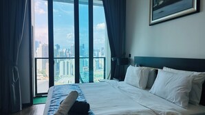 Ein Hotelzimmer mit einem großen Bett, Blick auf die Stadt durch raumhohe Fenster und einem Gemälde an der Wand.