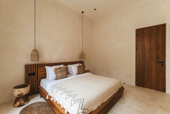 A bedroom with a wooden bed, two hanging lamps, a wooden door, and a round woven stool.
