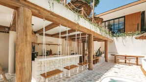 A poolside area with a stone-tiled floor, wooden swings, a stone wall, and a thatched roof. - Villa Bocce (Canggu)