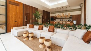 A modern living room with a sectional sofa, wooden accents, and a kitchen in the background. - Villa Bocce (Canggu)