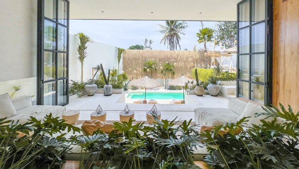 A modern indoor pool area with a glass ceiling, surrounded by tropical plants and furnished with white sofas and tables. - Villa Bocce (Canggu)