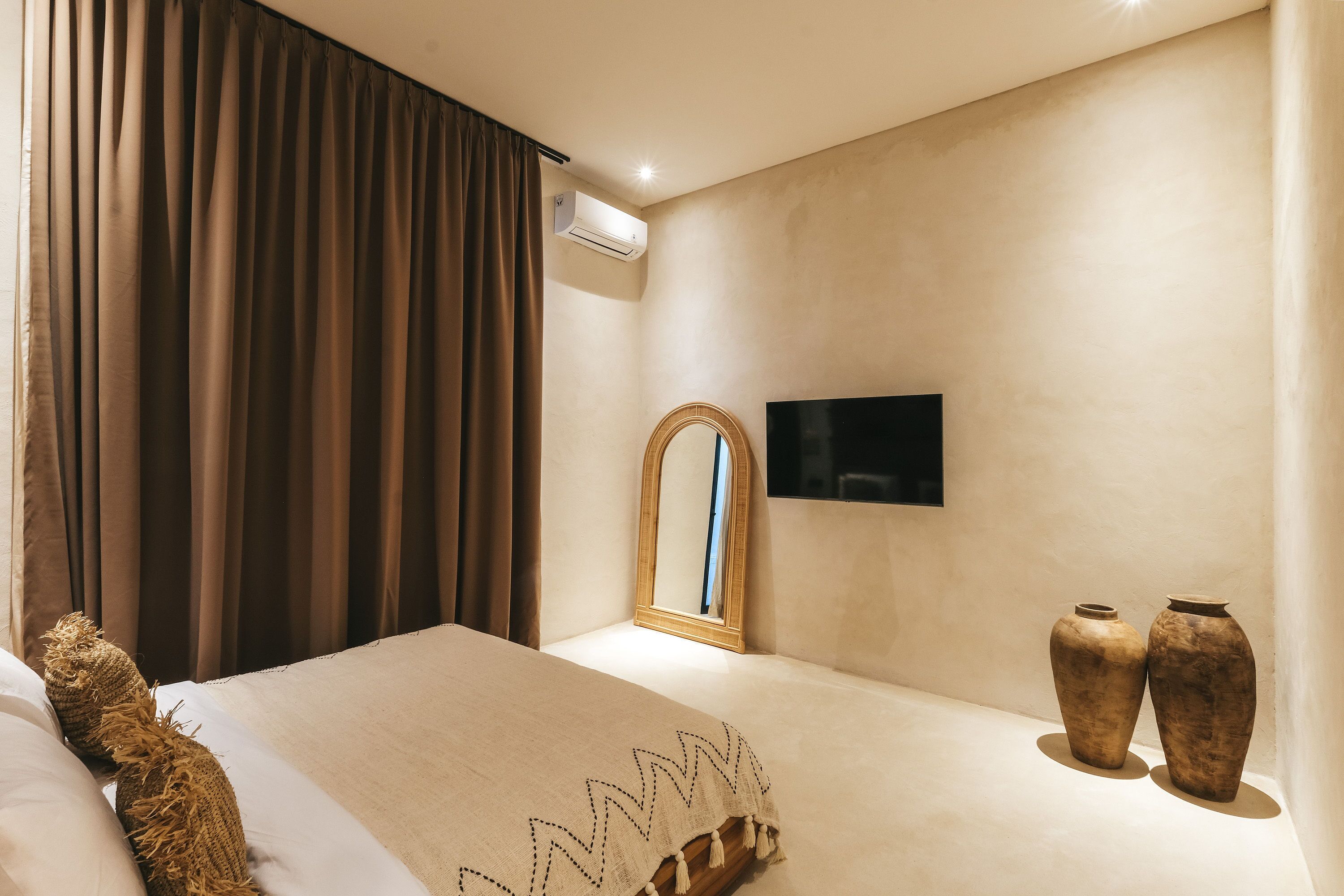 A hotel room with a bed, a flat-screen TV, a mirror, and two vases.