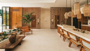 A modern kitchen with a long island, wooden chairs, and hanging rattan lights. - Villa Bocce (Canggu)