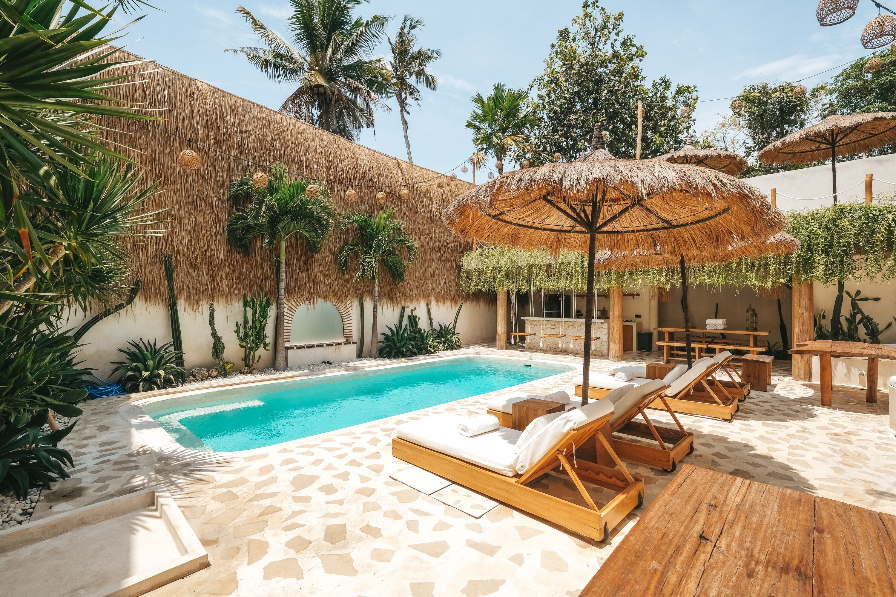 A poolside area with lounge chairs, a thatched umbrella, and a stone-tiled floor.