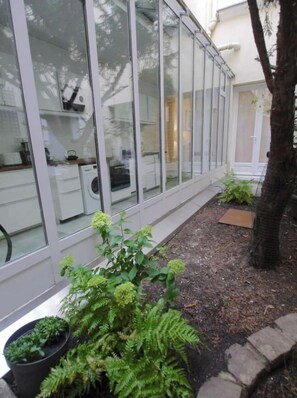 A modern kitchen with large glass windows, a washing machine, and potted plants. - Marais, Rue Volta, sleeps 4, with air conditioning – 1 bedroom (Paris)