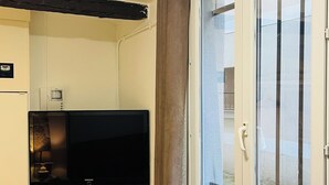 A room with a flat-screen TV on a stand, a radiator below the window, and a door with a view of the outside. - Arts-et-Métiers: 5 minutes walk from rue Rambuteau (Paris)