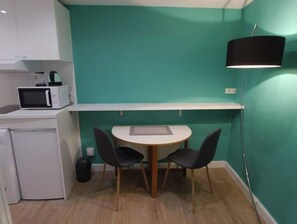 A compact kitchen with a microwave, a small refrigerator, a table with two chairs, and a black pendant light. - Arts-et-Métiers: 5 minutes walk from rue Rambuteau (Paris)