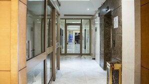 A modern hotel corridor with glass doors, marble flooring, and a view into the interior. - Wasan Suites Furnished Apartments (Riyadh)