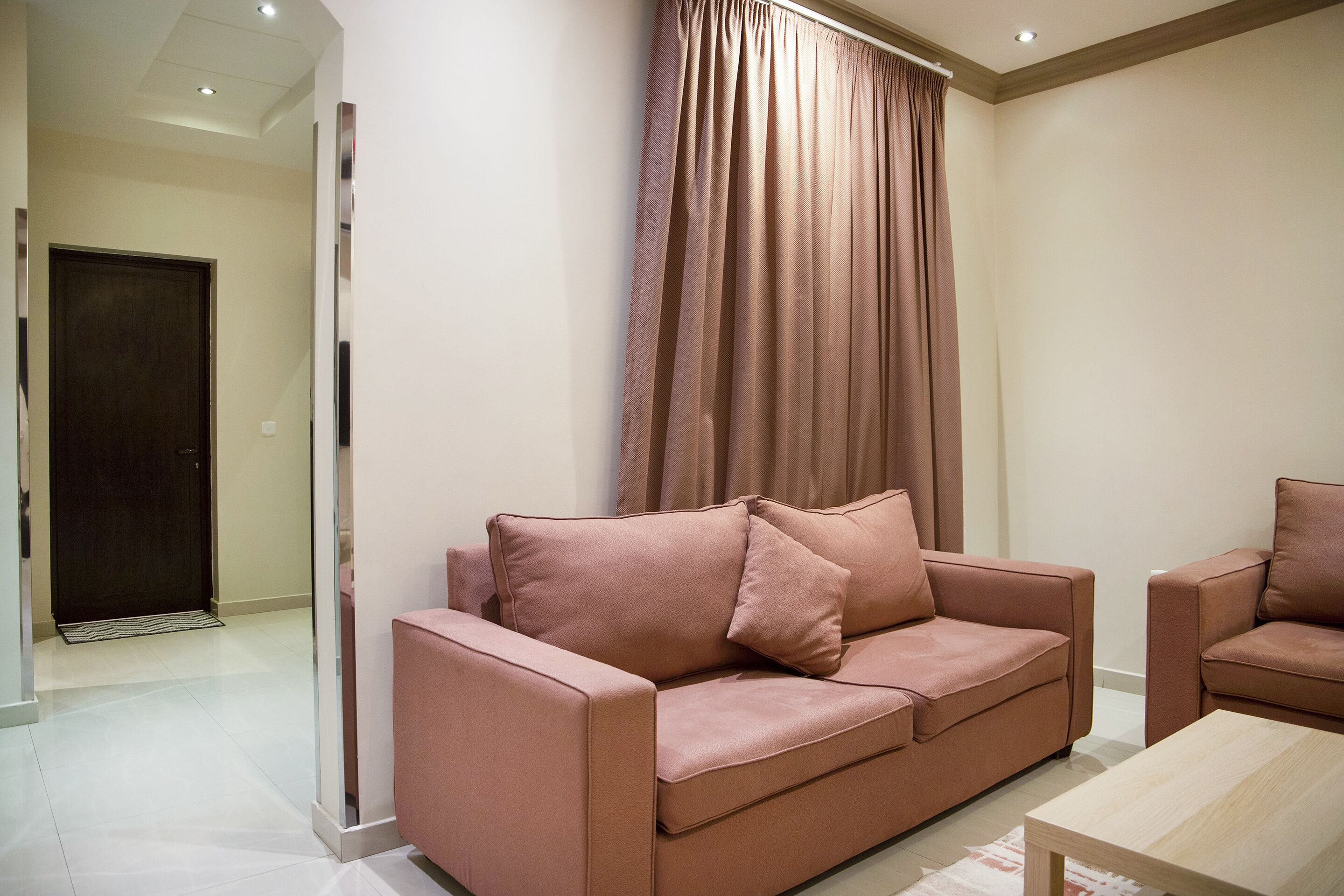 A modern living room with a sofa and armchairs, a wooden coffee table, and a large window with curtains.