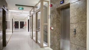 A modern hallway with glass doors, a marble wall, and an elevator. - Wasan Suites Furnished Apartments (Riyadh)