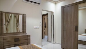 A modern hotel room with a large bed, a wooden wardrobe, a mirror, and a door leading to another room. - Wasan Suites Furnished Apartments (Riyadh)
