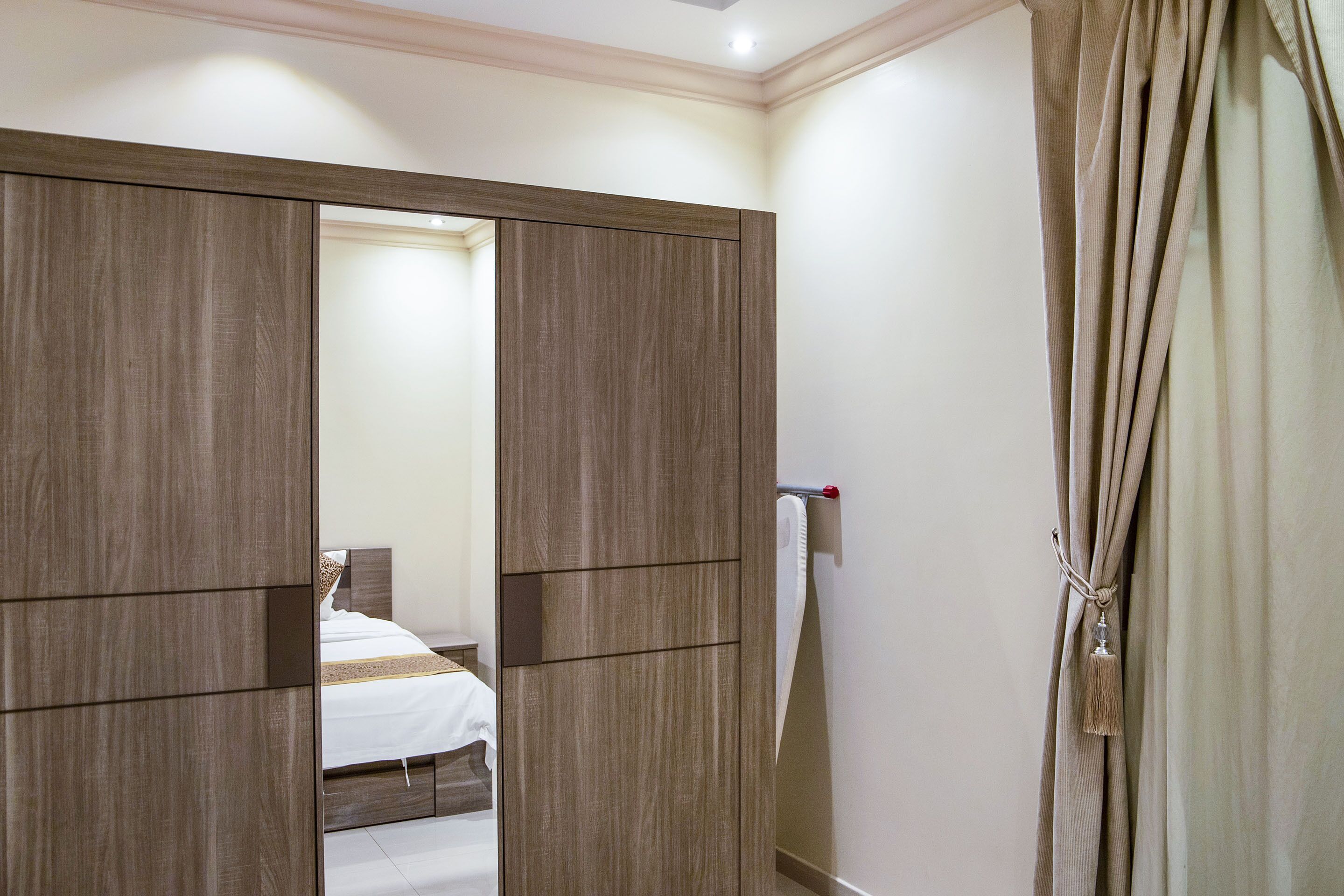 A bedroom with a wooden wardrobe, a bed with white bedding, and a curtain with a tassel.