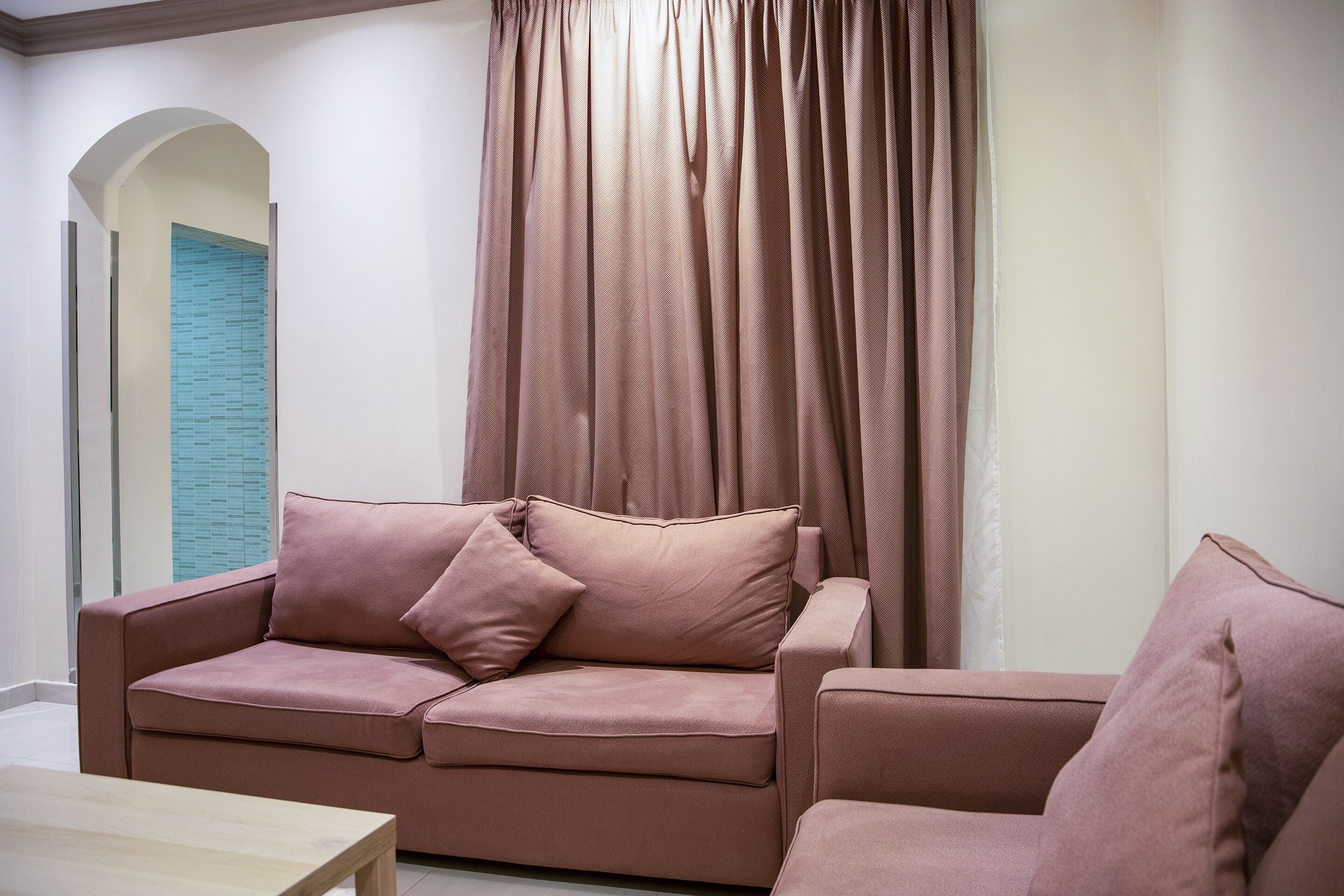 A living room with a sofa and armchair, a wooden coffee table, and a window with curtains.