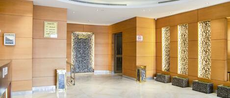 A spacious lobby with a marble floor, a reception desk, a wall-mounted information board, and a no-smoking sign.