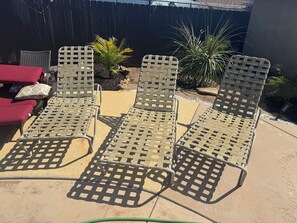 Eine Terrasse mit drei Metallstühlen und einem roten Sofa.